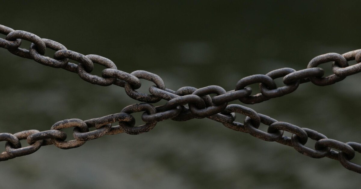 Close-up of crossed rusty chains over a blurred green background.