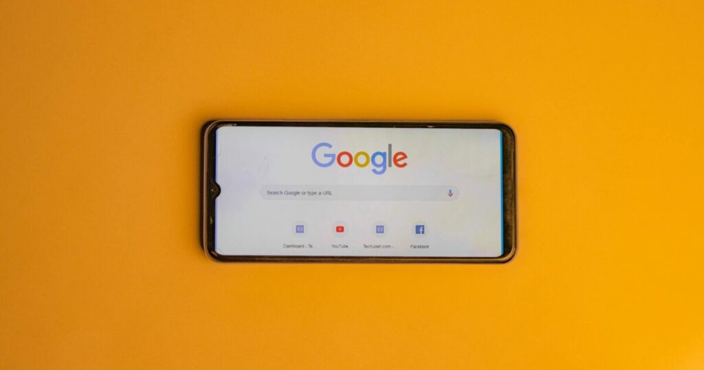 Smartphone displaying Google search page on a vibrant yellow background.