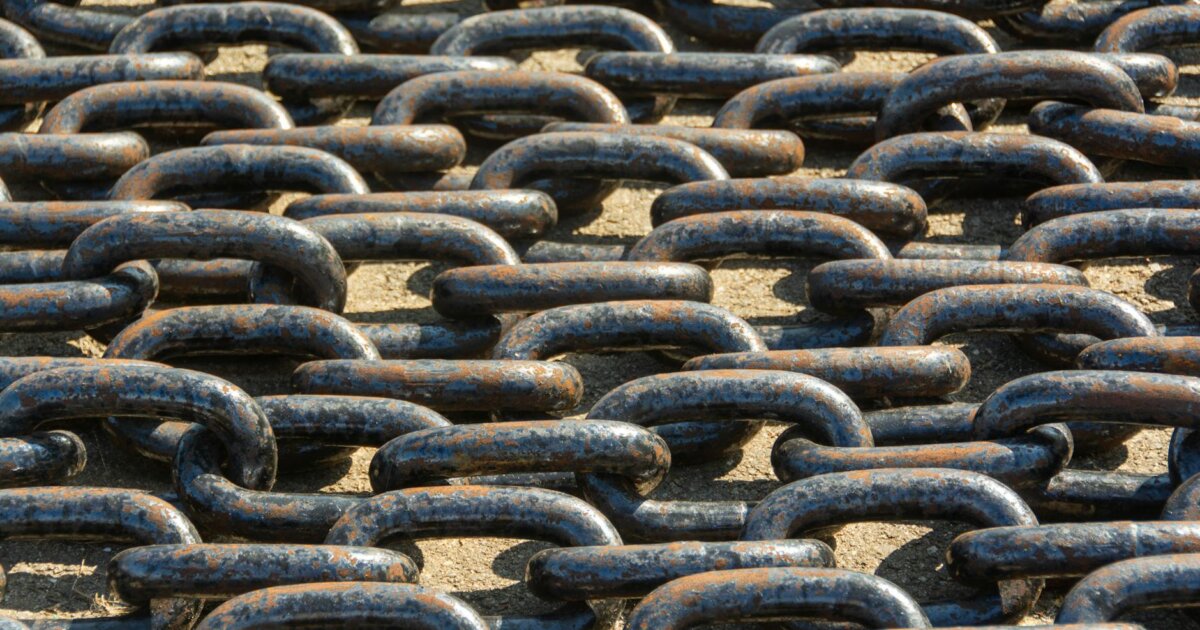 Detailed view of rusty metal chains arranged outdoors in sunlight.