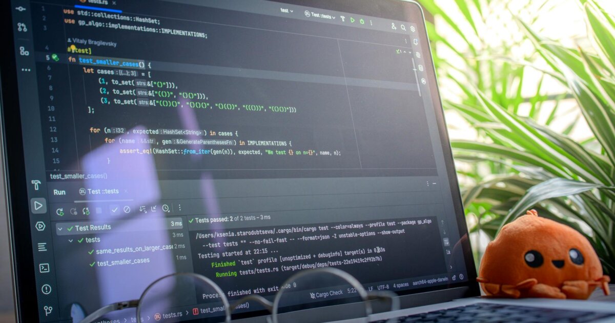 Open laptop displaying code next to a plush toy, set in a bright room with plants.