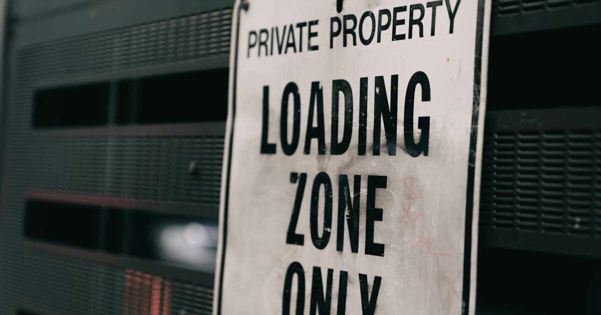 Close-up of a private property loading zone only sign with urban backdrop.
