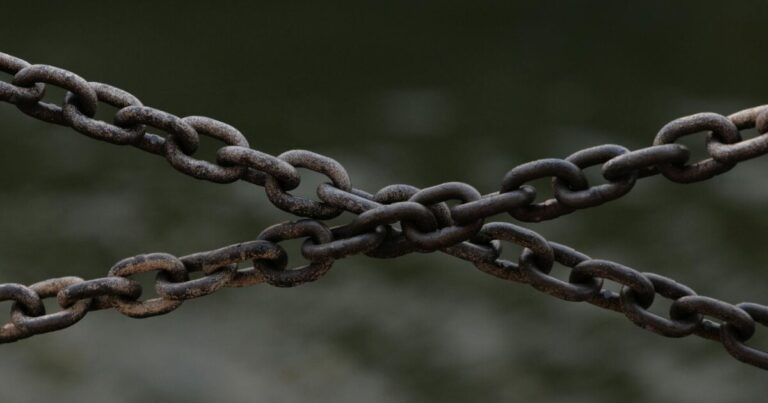 Close-up of crossed rusty chains over a blurred green background.