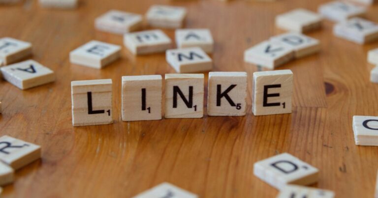Scrabble tiles arranged to spell 'LINKE' on a wooden table, surrounded by scattered letters.
