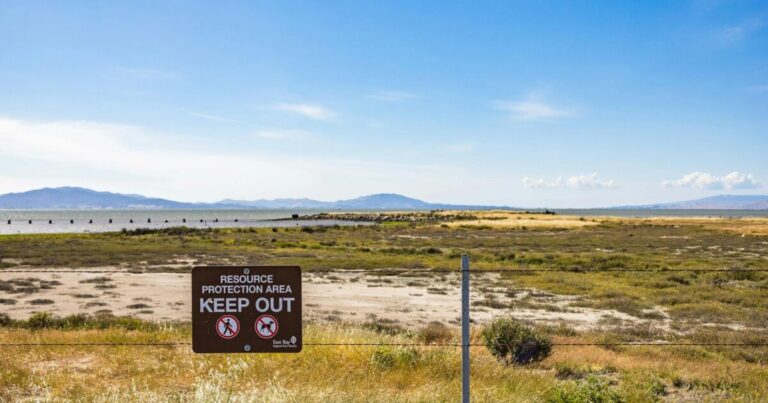 Wide view of a protected natural area with a 'Keep Out' sign and distant mountains.