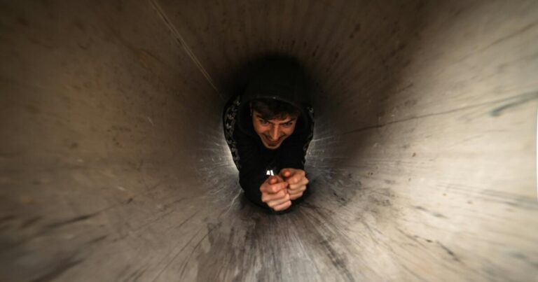 Young man crawling through a dimly lit metal tunnel, capturing a playful and adventurous moment.