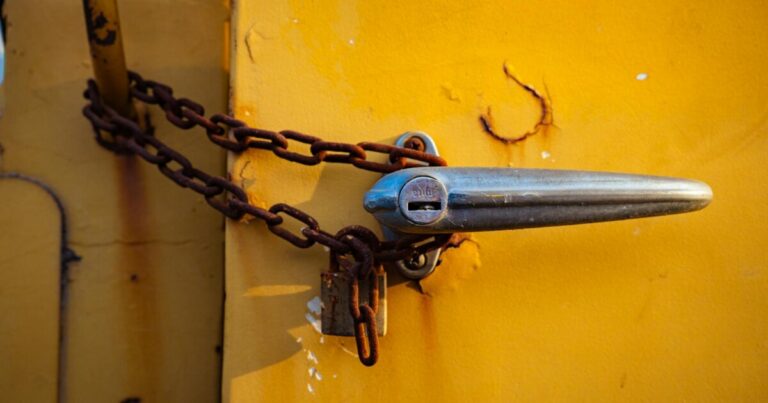 Close-up of a rusty chain securing a chrome handle on an old yellow metal door.