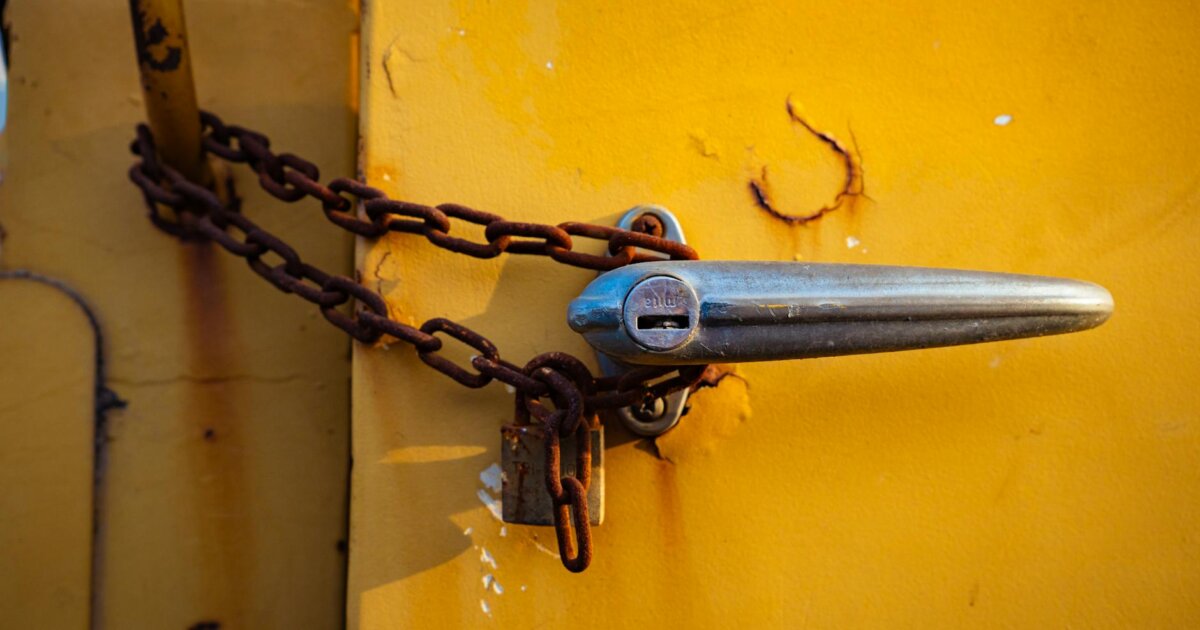 Close-up of a rusty chain securing a chrome handle on an old yellow metal door.