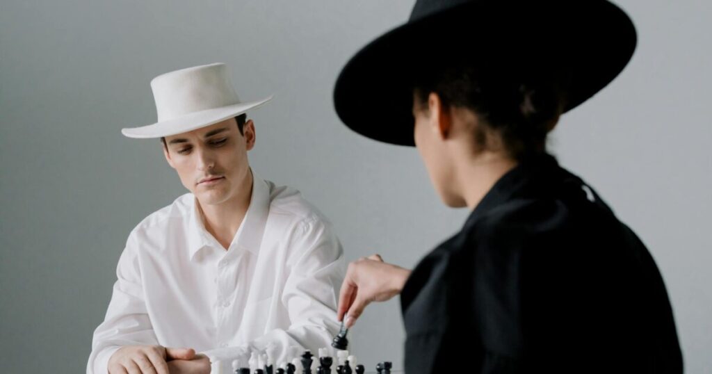 Two adults in contrasting outfits engage in a strategic chess game, showcasing style and focus.